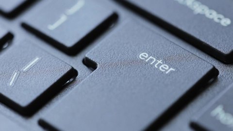 Finger presses the enter key on a modern black desktop pc keyboard. Hitting enter on computer keyboard, extreme closeup, detail