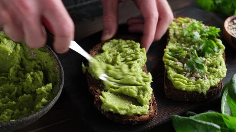 Preparing avocado toast. Male hands spreading mashed avocado on toasted whole grain rye bread. Vegan food, clean eating, dieting concept