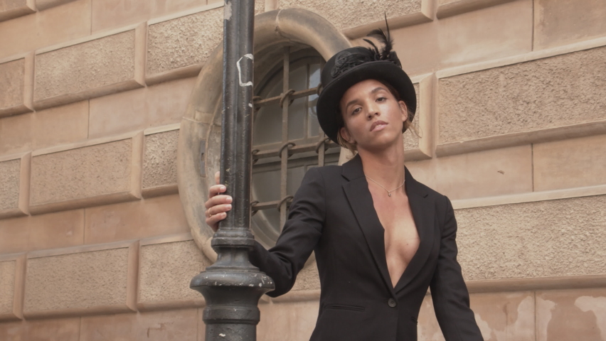 Medium Slow Motion Handheld Shot Of Young Dancer In High Heeled Boots, Jacket And Top Hat Moving Around Streetlight