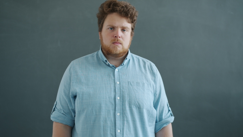Slow motion portrait of aggressive young man crossing arms and looking at camera with angry face standing against gray background. People and emotions concept. | Shutterstock HD Video #1069906279