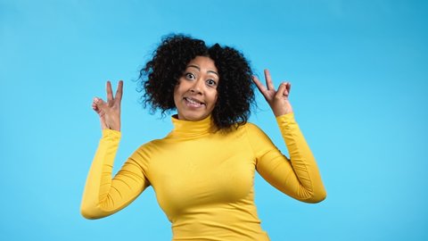 Mixed race woman showing with hands and two fingers air quotes gesture, bend fingers isolated over blue background. Not funny, irony and sarcasm concept.
