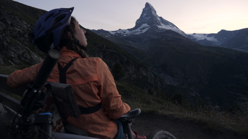 Mountain biker sits on bench and looks at stunning Alpine scenery.
