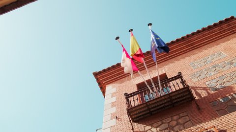 Three flags waving on a flagpole on the old building of touristic town of Toledo. Castilla–La Mancha, European Union and flag of Spain, view against blue sky at sunny day. Europe. Spain