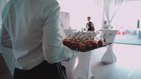 male waiter serving catering on banquet and holding meat snack on plate