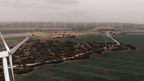 Drone point wide angle aerial view of moving turbines of windmills. Wind energy converter into electricity. Panoramic real time video of cultivated farm lands during gloomy day. Europe, Spain