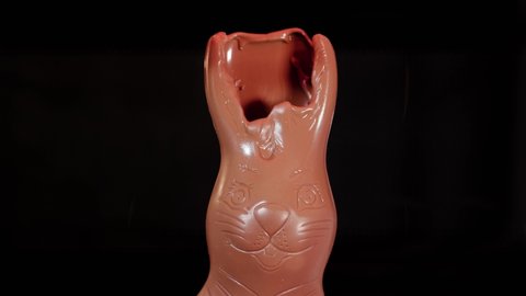 Chocolate bunny figure melting in heat, face slowly melting down, dark background, chocolate rabbit with big ears