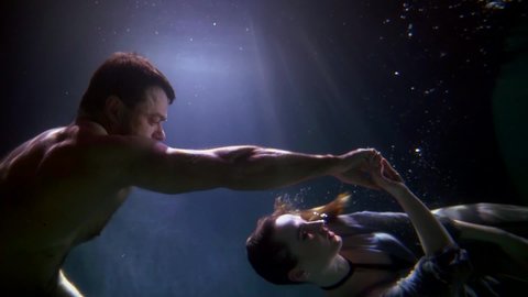 loving pair is dancing underwater, unusual romantic date of young lovers, slow motion subaquatic shot