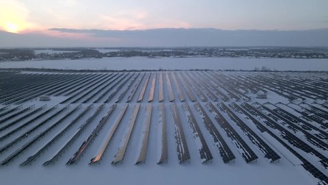 Renewable green energy and electrical technology. Field of Solar Panels Stands in a Row in the Fields for Power Production at winter sunset. Drone fly over Solar Farm. Green energy concept.