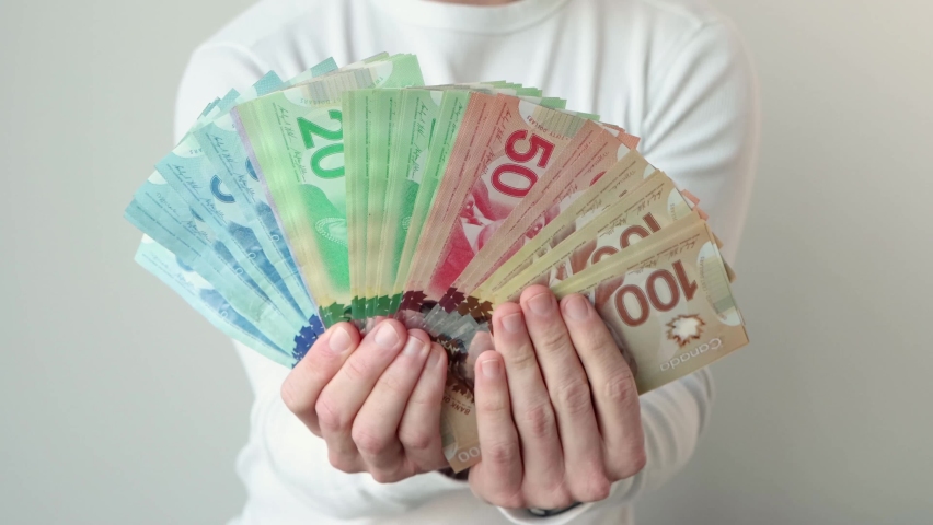 Man holding many Canadian dollar bills with multiple values, colourful notes