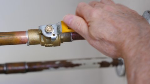 Plumber turning water shut off valve. Copper plumbing pipe with brass water supply valve and yellow stopcock handle.