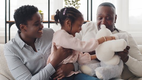 Happy three generation afro american family at home play with teddy bears close-up portrait. Little black girl daughter granddaughter having fun with adult mother and grandfather gives five with hand