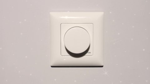 a man with his hand rotates the dimmer knob on the wall