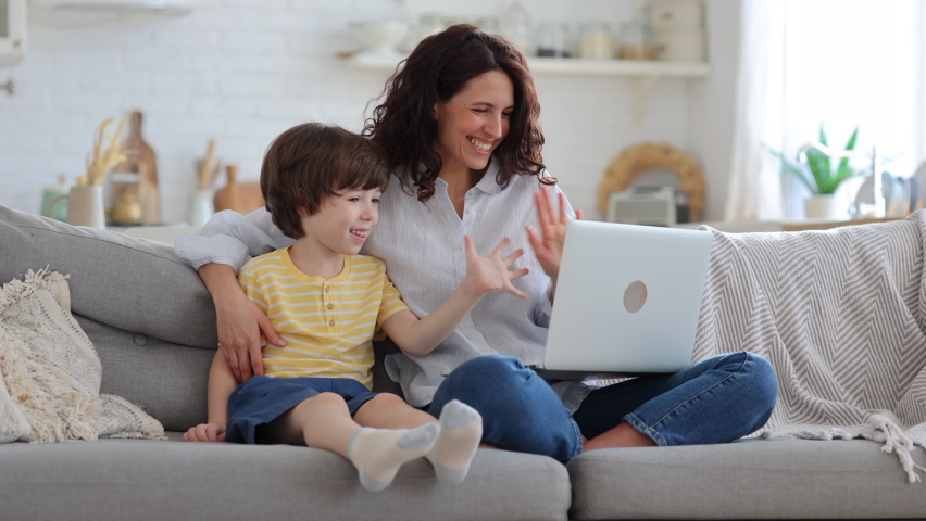 Family, lockdown. Happy mother and kid son greeting online, waving hands, looking at web camera laptop for video call sitting on couch at home. Smiling mom and child having fun talking in video chat . | Shutterstock HD Video #1069921252