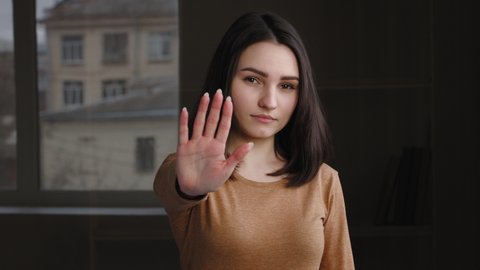 Portrait young girl brunette caucasian woman displeased angry lady offended sad model puts in front of her palm, makes stop gesture, shows refusal prohibition warning sign with hand, keep distance