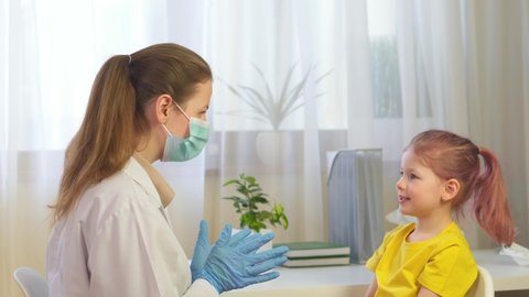 Cute little girl smiling at the hospital at the doctor's appointment. The pediatrician and the child laugh. The nurse gives five to the little patient. doctor in mask and gloves in hospital.