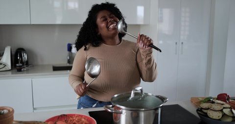 Black young african woman having fun cooking and dancing inside kitchen at home  库存视频