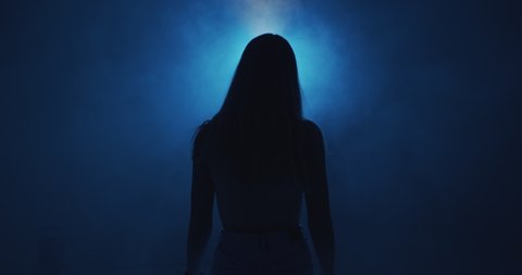 Mysterious female silhouette in blue light and smoke cloud at night. 4k video of young girl in haze