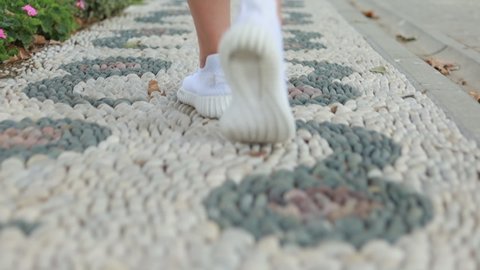 Female feet in white sneakers walk along the paths and sidewalks of city streets and parks
