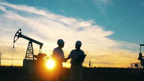 Two engineers working at oil field surrounded by oil pumpjacks