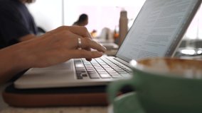 Remote work concept. Close up of female hands typing on a laptop and drinking coffee.