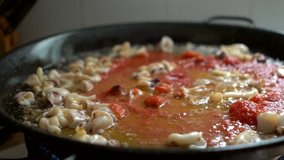 adding crushed tomato to fry during the preparation of fideua in paellon typical Spanish food