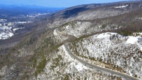 Aerial drone video footage of a snowy, blue sky mountain valley road highway through the mountains in the Appalachians on the Shawangunk ridge, in new York state