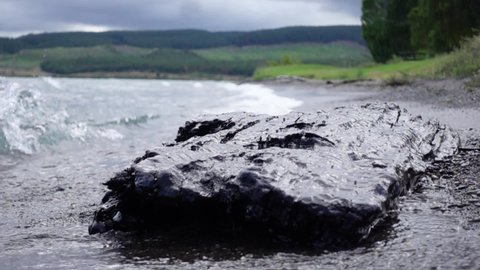 Wave splashes on large dark rock on shore of Lake Taupo, slow motion