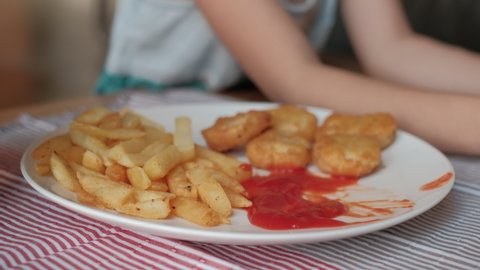 Close-up VDO show Child's eating fast food and forcing Joystick to play video games, White dish with french fries, nuggets, and ketchup. Online entertainment technology makes kids addicted.