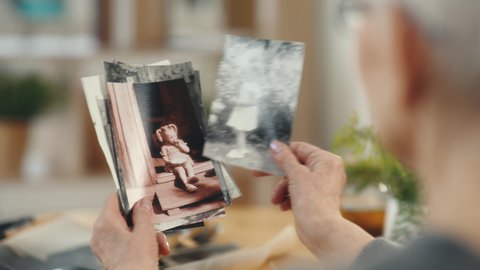 Senior woman looking at old photo album close-up. Adult female holding nostalgic memory of small kid at cozy modern home. Casual elderly life and wrinkled skin of hands. Biography or history concept