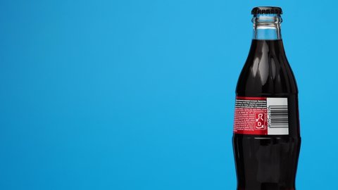 Estonia, Tallinn - March 2021: glass bottle coca-cola soda zero sugar drink rotating on isolated blue background.