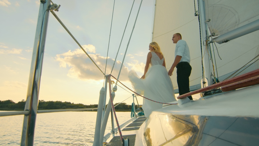 Newlyweds stand on a bow of a sailing yacht like in Titani. The bride put her head on the groom