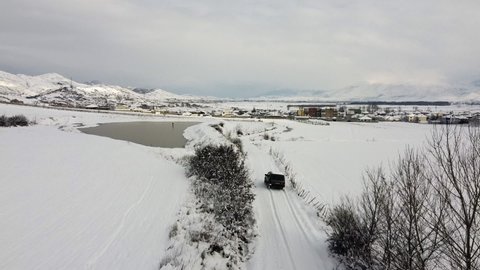 An aerial drone video of a Russian made 4x4 off-road Lada Niva car driving along a snow-covered dirt road in Southern Albania early one winter morning.