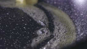 Butter melting sizzling in frying pan on stove. Slow-motion close up