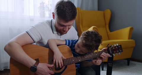 The father and the little boy, a nice and handsome son, play the guitar and learn musical chords. Love, affection for children. The father gives time to the son during a pandemic, self-isolation.
