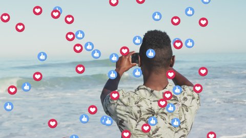 Animation of red heart love and like digital icons over man filming sea with smartphone on beach. digital interface, social media and global networking concept digitally generated video.