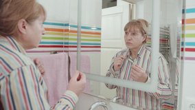 Senior Frustrated woman looks in the mirror and plucks a grey hair from her head. Concept video of senior woman getting old