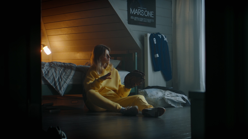 WIDE Attractive Caucasian teenager girl playing baseball catch with herself in her attic bedroom at home. Shot with 2x anamorphic lens