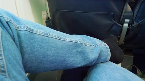 FPV of male passenger sitting on cabin chair in plane during flight. Close up of legs of relaxed passenger.