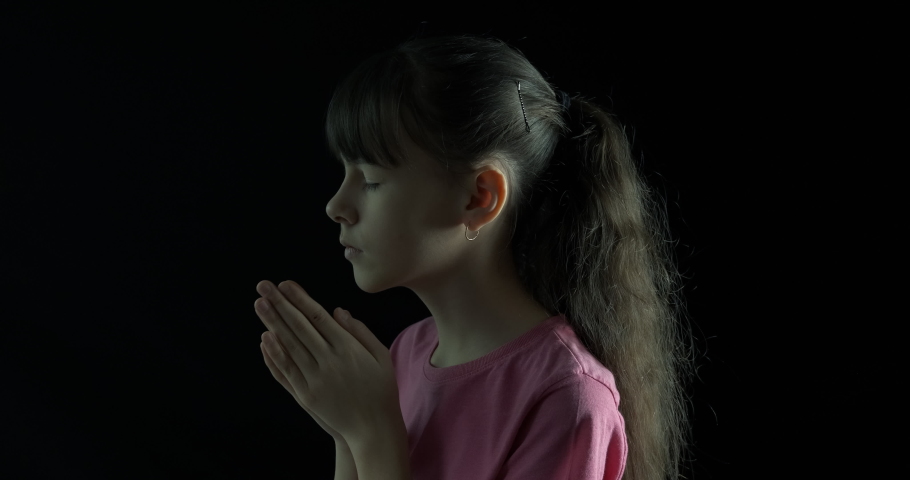 The child is praying. Teenage girl praying on a black background.