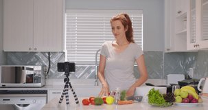 Adorable woman talking recording cooking video at kitchen interior. Beautiful young female blogger preparing healthy food use fresh organic vegetable.
