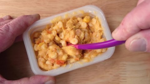 Stirring a toddler meal of macaroni and cheese then taking a spoonful.