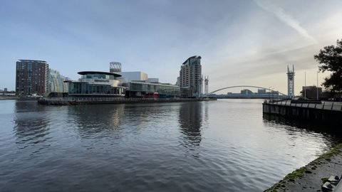 Salford Quays England. March 25, 2021. Timelapse looking across the water towards The Lowry Theatre with modern buildings and a modern bridge. 