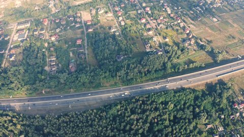 Small neighborhood houses near a large freeway with traffic - the aerial drone shot. Small neighborhood houses in a green modern village under a white cloud at summer day near a large freeway.