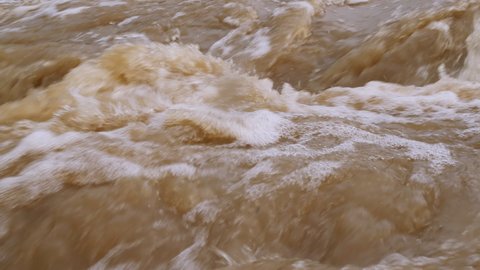 Raging river with dirty water. Crowded river overflows its banks. Natural disasters, extreme weather. Disaster flood deluge and water flow in close up.