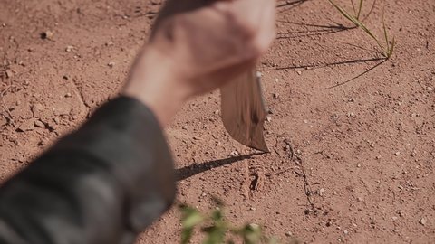 A man writes something with a knife on the dry ground. The knife is quite large. Close-up hand shots