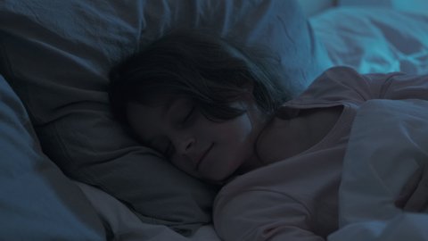 Sleeping child. Night rest. Sweet dreams. Kid bedtime. Cute small girl lying in cozy soft bed tossing turning in dark home bedroom with blue moonlight.