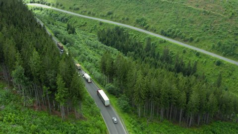 Aerial view of the road with driving cars and truck in the mountains with high green fir, foliar, pine or spruce trees.