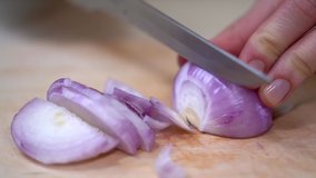 Closeup view of a woman hands cut red onion into slices with a knife. Red onions ring