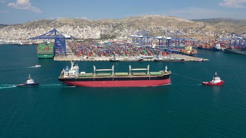 Aerial drone video of cargo carrier tanker leaving industrial port of Perama with the help of tug boats for Mediterranean destination, Attica, Greece