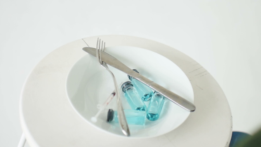 Woman is going to eat from white plate with glass ampoules with blue liquid inside, vaccination concept, top view